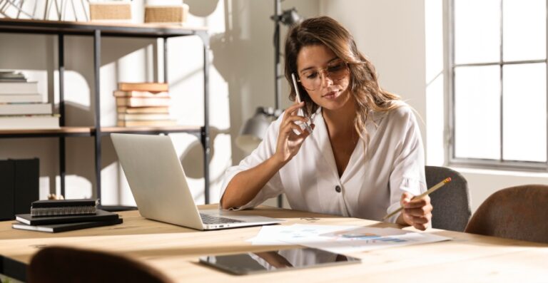 Mulher analisando documentos fiscais em escritório, com notebook e gráficos sobre a mesa — representando controle e organização tributária.